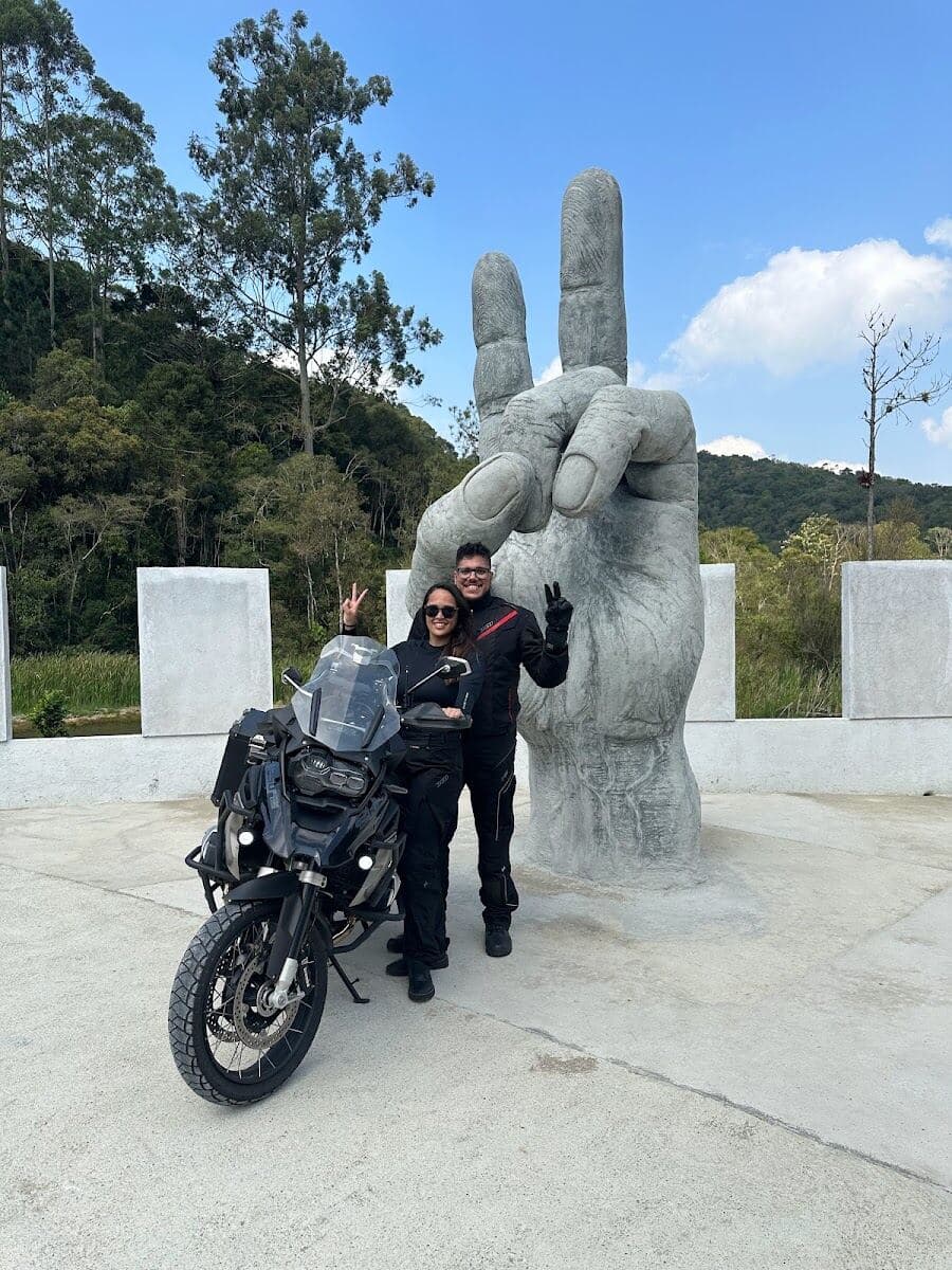 Com a moto ao lado da escultura da mão fazendo o sinal de paz